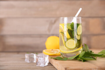 A glass of lemon cucumber water and fresh lemon fruit, ice cubes and mint leaves on a cutting board