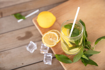 A glass of lemon cucumber water and fresh lemon fruit, ice cubes and mint leaves on a cutting board