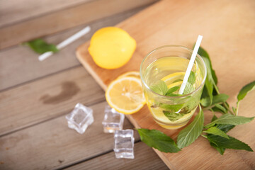 Iced lemon mint water on the cutting board and fresh lemon fruit, ice cubes and fresh mint leaves next to the glass