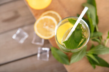 Iced lemon mint water on the cutting board and fresh lemon fruit, ice cubes and fresh mint leaves next to the glass
