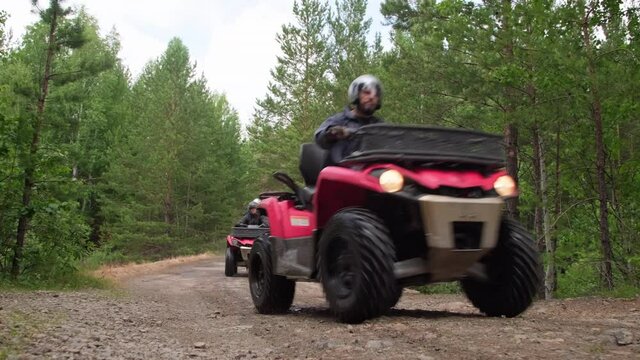 Slowmo tracking ground level shot of people in helmets driving quad bikes along forest road