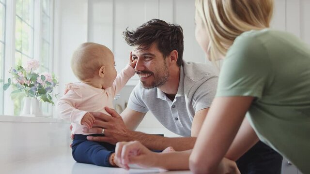Family with baby daughter having fun playing game sitting in kitchen together - shot in slow motion