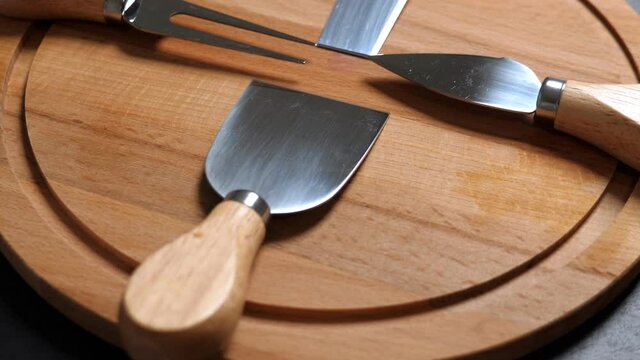 Cheese knifes and fork on wooden platter. Rotating