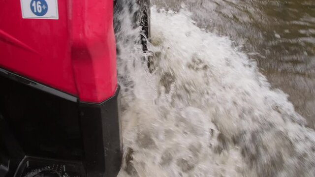 Close up handheld tracking shot of red quad bike driving through water in rough terrain