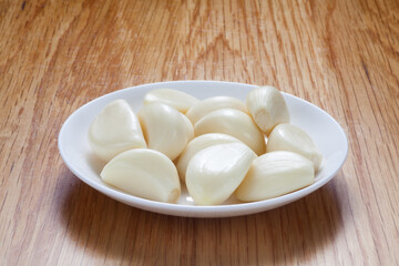 Fototapeta na wymiar Peeled garlic in a white plate on wooden table.