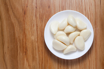 Fototapeta na wymiar Peeled garlic in a white plate on wooden table. Top view.