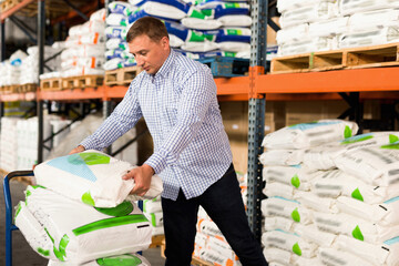 Satisfied positive Man choosing compost soil in plastic bags in hypermarket .