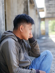 An Indonesian teenager boy worried sitting with a hand on the head. portrait of Asian young man depressed and sad.
