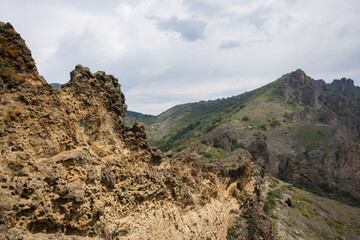 Wind-eaten steep slope of the volcanic mountain on the background of clouds and the Kara-Dag mountain range on the Crimean Peninsula