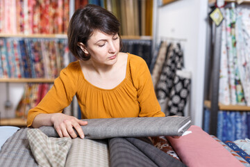 Obraz premium Pensive woman choosing textiles for dressmaking in fabric shop..