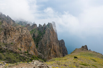 Mountain slope with flowers and peaks of Kara-Dag mountains in the fog of clouds on the Crimean Peninsula
