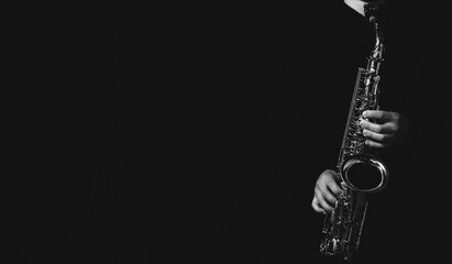 Grayscale shot of a cool and handsome guy playing his saxophone isolated on a dark background - obrazy, fototapety, plakaty