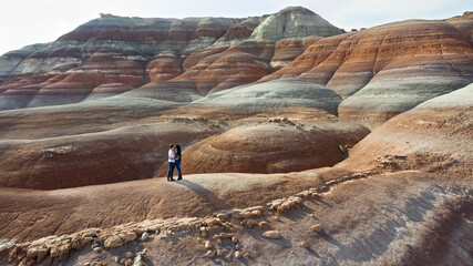 Couple kissing in a desert landscape resembling planet Mars. Rock layers with orange, red, blue, purple, and orange hues in the sediment can be seen 