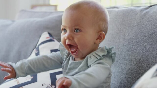 Cute baby girl sitting on sofa smiling and laughing as she gets excited - shot in slow motion