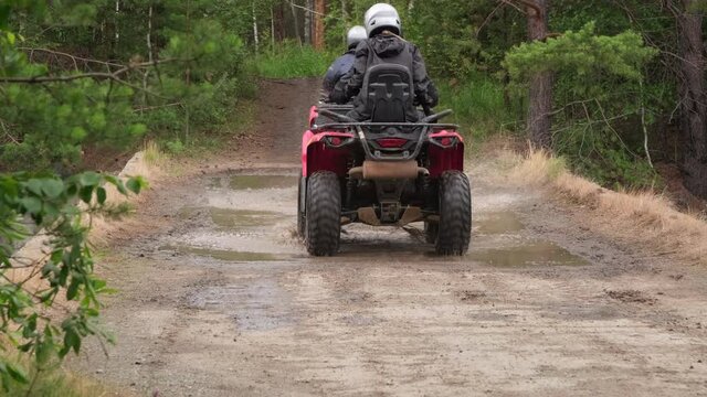 Lockdown shot of people driving ATVs through puddle on forest road in rough terrain
