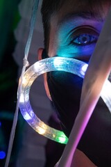 Person’s face with a COVID-19 (coronavirus) mask on for safety with colorful light tube and cloth materials in an abstract space
