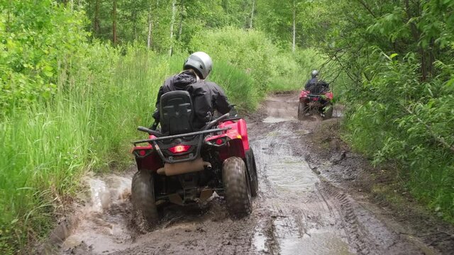 Slowmo tracking of people driving quad bikes through mud and puddles on forest road in rough terrain