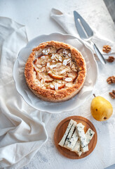 pie with dor blue cheese, pears and almond, whole round on a plate on a white table. Sugarless. Selective focus.