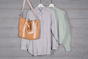 A bag, blouse and shirt is hanging on hanger in the clothes store on the wooden wall background.