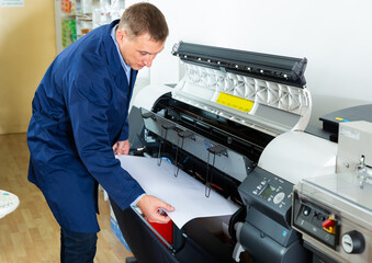Obraz premium Worker loads new roll of paper into the plotter. High quality photo