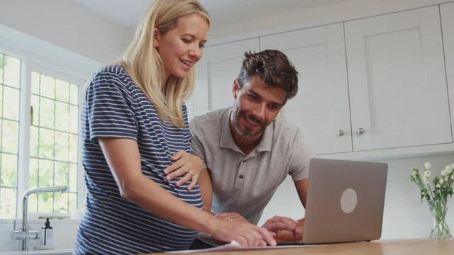 Couple with pregnant wife at home buying products or services online using laptop - shot in slow motion