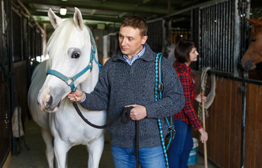 Portrait of man farm worker standing near white horse at stable