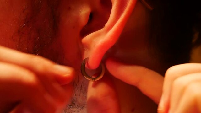 A young guy inserts a beautiful earring into his ear close-up