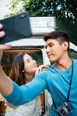 Couple taking selfie photo with smartphone standing by car at camping site.