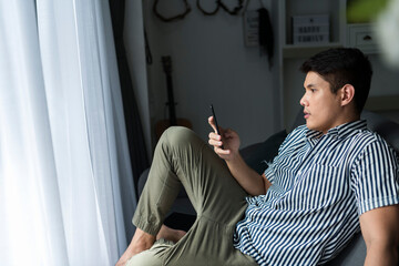 Asian man sitting on sofa using smartphone at home.