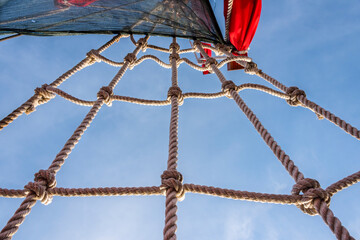 Rope ladder on sailing ship leading to the mast of the ship with sails against the sky and clouds