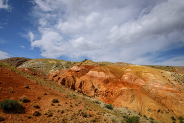 Fototapeta premium Martian landscape, natural landmark of Altai Republic. Mountains colored red, yellow, and orange against a blue sky with white clouds.