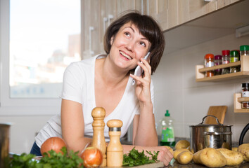 Positive brunette woman talking on her smartphone at kitchen