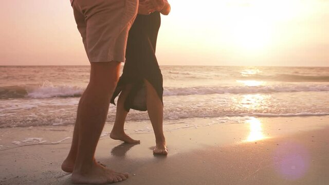 Couple walking on sandy beach barefoot stopping kissing at sunset. Dating, romance, courtship concept.