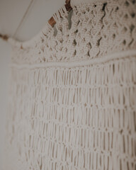 Wall panel in Boho style made of cotton threads in natural white color using the macrame technique. Home decor and wedding decoration.Hand made natural cotton macrame decoration hanging on white wall.