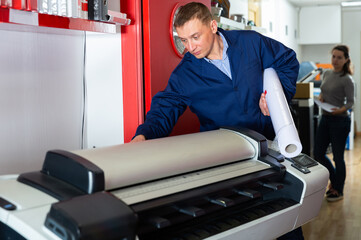 Worker loads new roll of paper into the plotter. High quality photo