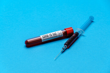 Syringe And Plastic Test Tube With Blood Sample over blue background with copyspace