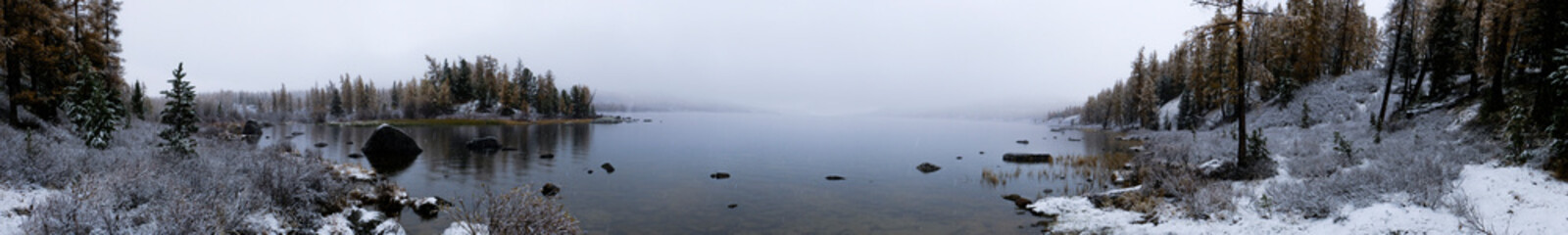Beautiful mountain lake in autumn during snowfall. Bukhtarminskoe lake in East Kazakhstan. Tourism, travel concept in Kazakhstan. Autumn forest nature. Beautiful fall nature. Outdoor landscape.