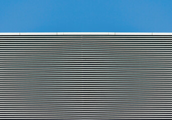 Obraz premium striped wall of a gray tall building against a blue clear sky