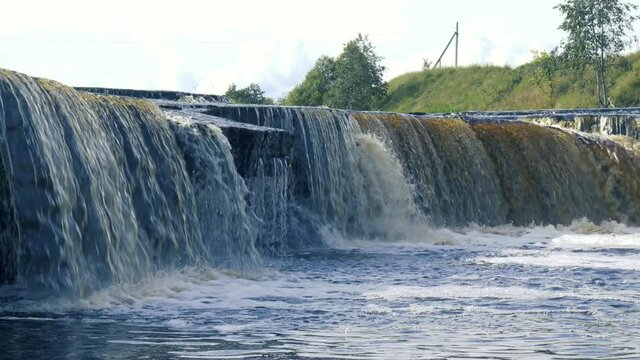 Waterfall, water flowing from the river falls down. A stormy river with a brown hue.