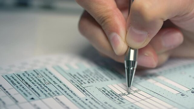 Closeup of unrecognizable female hand holding pen filling out printed tax declaration form ticking boxes
