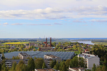 The urban industrial landscape with a factory, residential buildings and pipes on the horizon in the summer in Russia. A man-made landscape. An industrial city with green trees. 