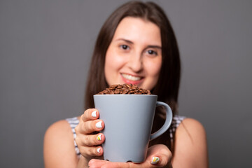 Portrait of a young woman holding a mug with coffee beans.