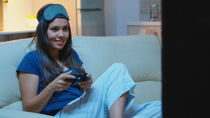 Woman sitting on sofa playing video games, smiling relaxing enjoying the evening. Excited determined gamer using controller joysticks keypad playstation gaming and having fun winning electronic game