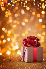 Gift box with red ribbon against magic golden lights and bokeh background. Christmas holiday greeting card.