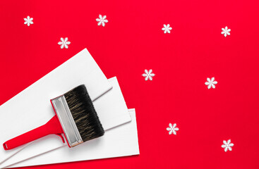 A large new red plastic paint brush in metal edging for painting and white wood planks and snowflakes on a red background. Banner with copy space for a hardware store or art shop