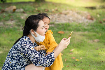 Mother and daughter sitting at field using smartphone.