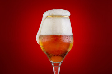 Glass of beer with foam cap isolated on red background,