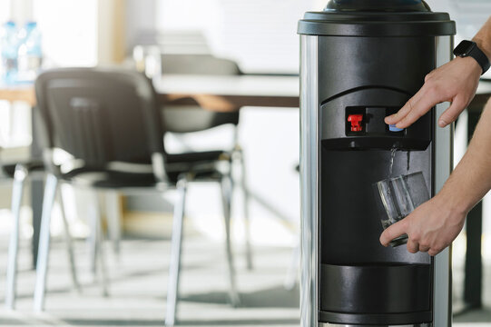 Water dispenser in the office, with hand filling a glass of water