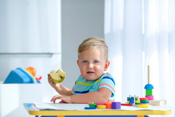 A little boy 2 years  eats an apple and is played with wooden balls. Educational logic toys for children. Montessori games for child development.