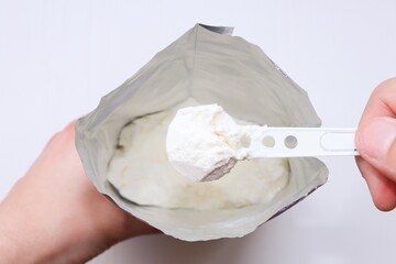 Plastic spoon with infant formula. A hand picks up infant formula from a package.